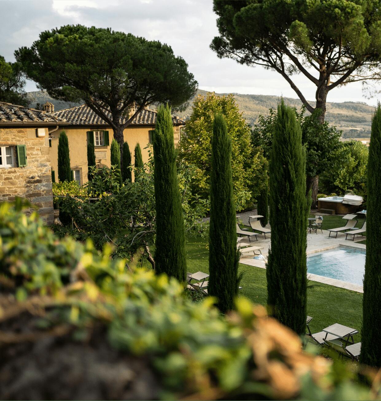 Traditional Tuscan villa surrounded by cypress trees and rolling hills, featuring a private pool and peaceful countryside setting.