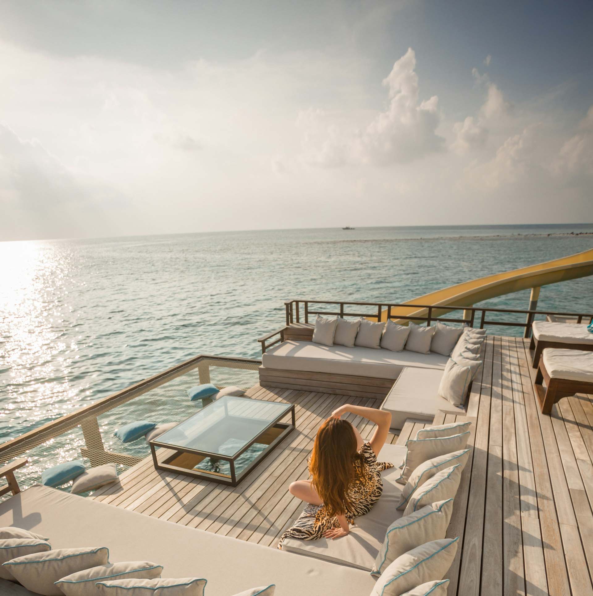 Woman lounging on a couch on deck of a luxury yacht overlooking the vista.
