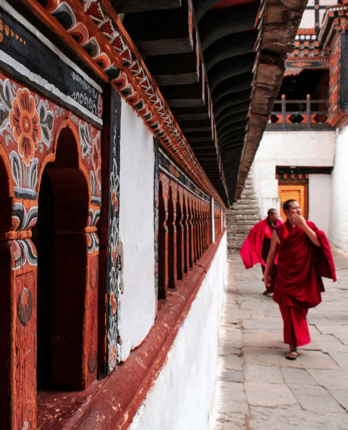 Colorfully robed monks walking along a beautifully decorated sacred corridor at Tiger's Nest Monastery in Bhutan.