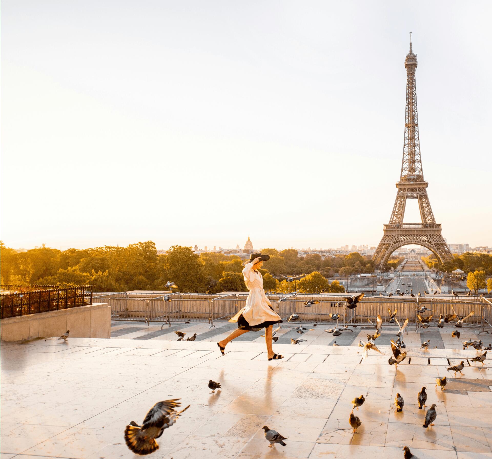A fashionable woman runs through a flurry of pigeons across the Trocadero with a breathtaking view of the Eiffel Tower in the background.