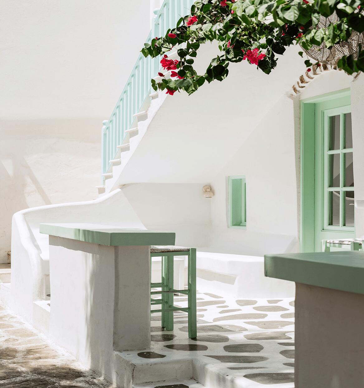 White sun dappled staircase on the exterior of a building draped with climbing flowers in Greece.