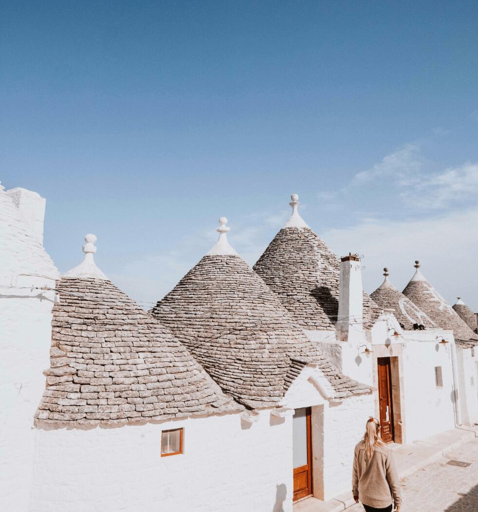 A woman strolls down a charming street lined with trulli in a picturesque Puglian village.