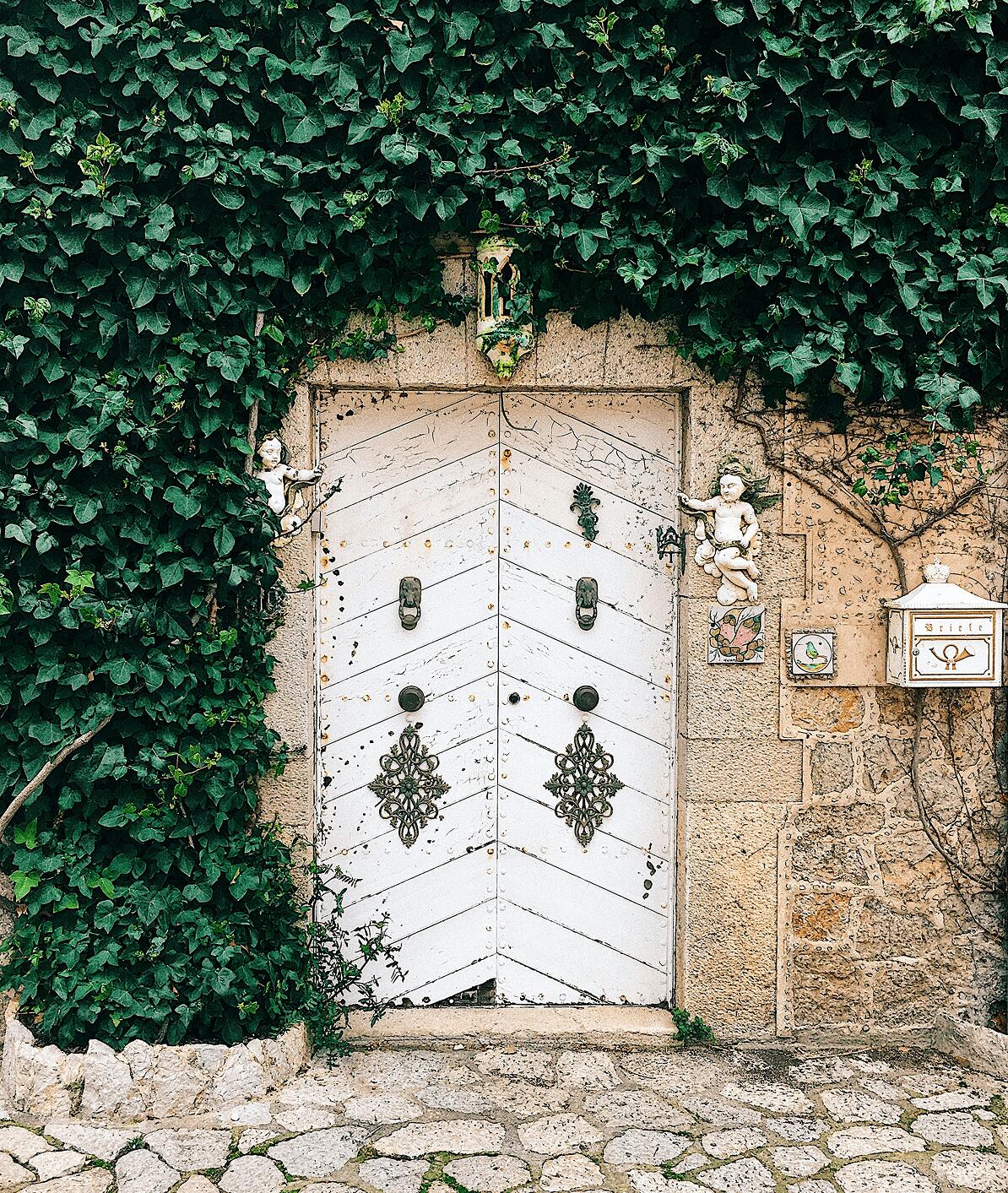 Rustic door in an old stone walll surrounded by lush ivy vines that have overgrown the surrounding wall on the island of Mallorca, Spain.